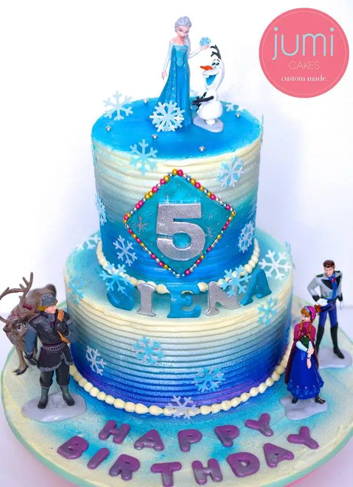 A two-tiered cake with store bought figurines of Frozen characters for a Frozen themed cake. Jumi Cakes. Source