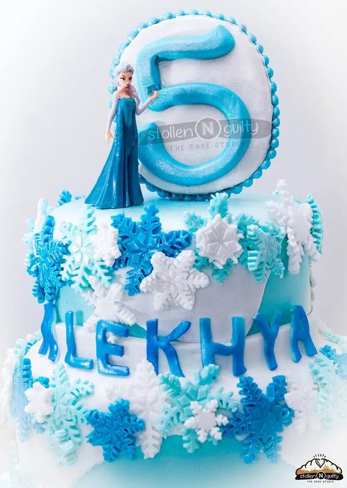 A regular two-tiered round cake decorated with white and blue fondant to create a Frozen themed cake. Stollen N Guilty .Source