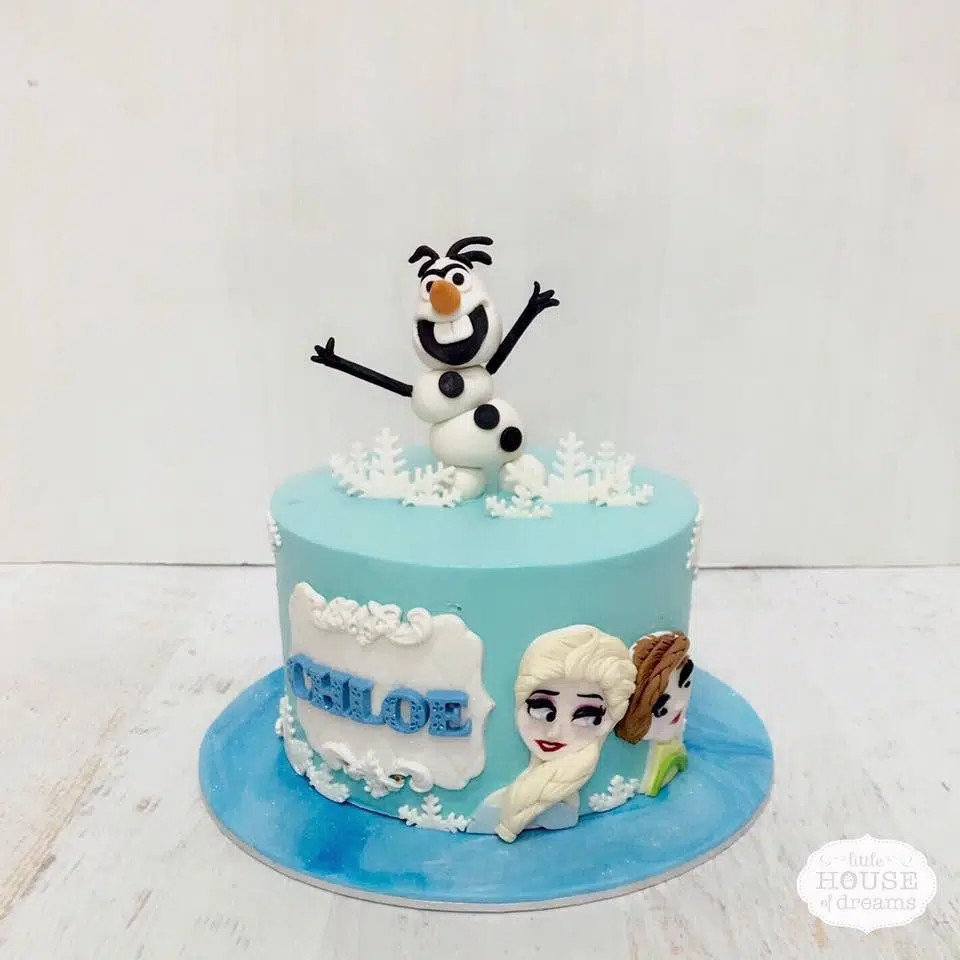 A Frozen themed round cake with edible Olaf figurine cake topper, 2D image of Elsa and Anna. Little House of Dreams.Source