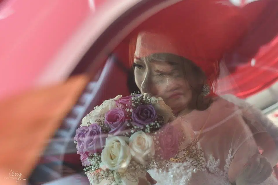 Bride tearing up as she leaves her parents' home in Malaysia, as mother's face is reflected in the car window. Photo by Qinghui Photography. Wedding photographers in Malaysia at Recommend.my